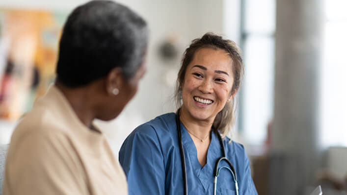 A smiling nurse sits and talks with a patient in the waiting room.