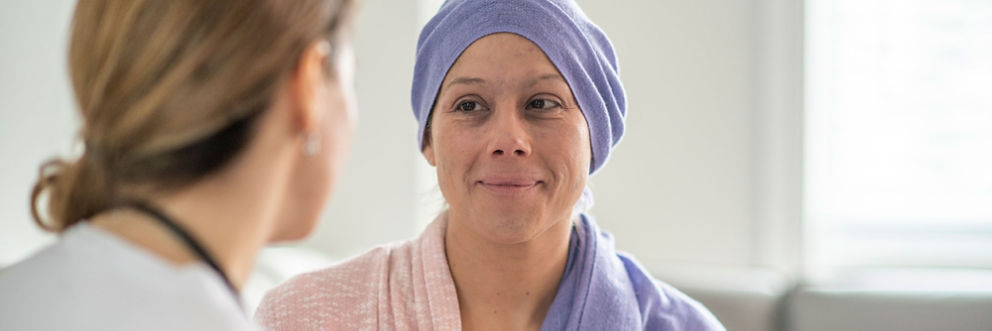A cancer patient with a beautiful headscarf smiles while talking with her doctor.