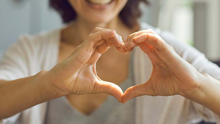 A smiling woman makes a heart shape with her hands.
