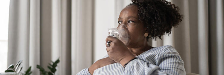 Woman breathing into a nebulizer mask with her hand on her chest.