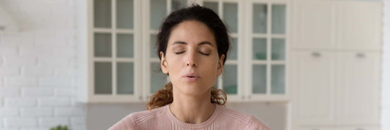 Woman closes eyes and opens mouth slightly while taking a deep breath to lower stress levels and keep her heart healthy