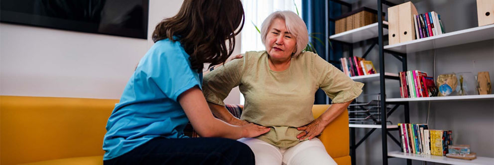 A woman touches her mother’s hip to confirm the location of hernia pain.