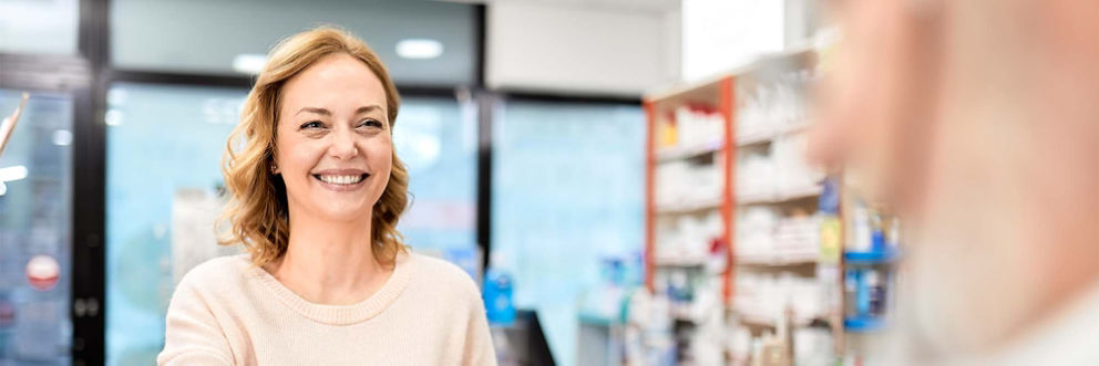 A woman standing in a pharmacy smiles as she talks with another man