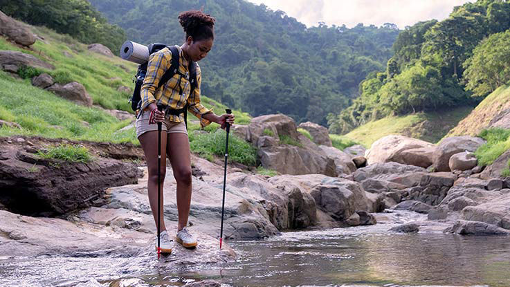 A woman crosses a stream during a hike.