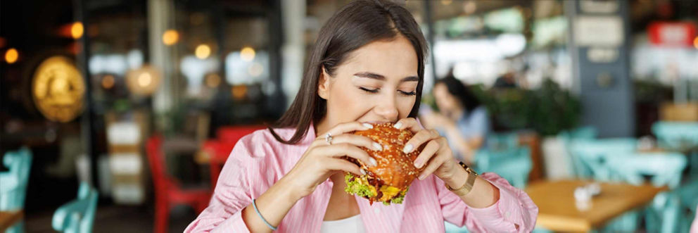 A woman takes a large bite of a hamburger.