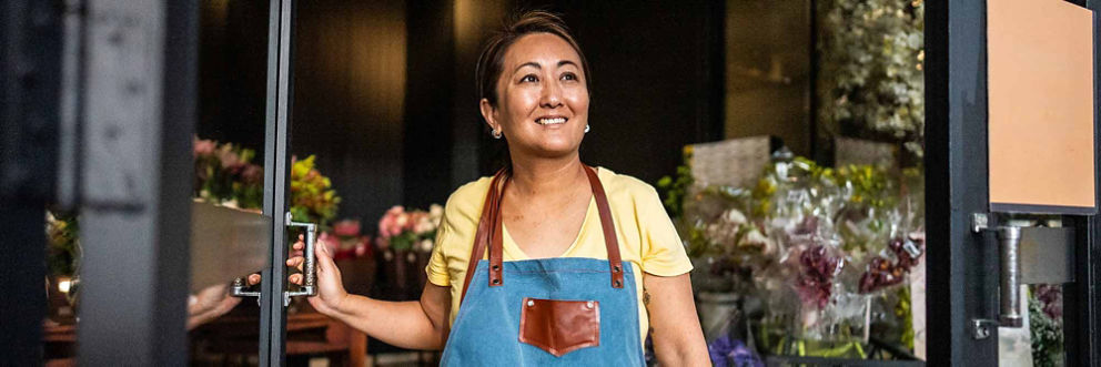 An owner of a flower shop stands in the front door of her business and looks out smiling