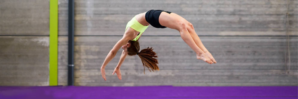 A woman does a backflip on a tumbling mat.