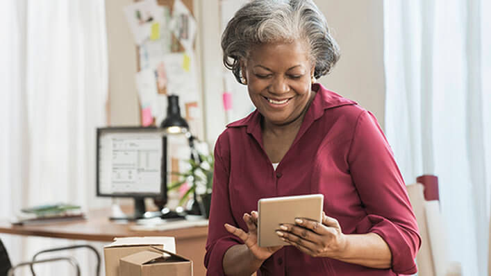 A woman smiles as she scrolls through a tablet in her home.