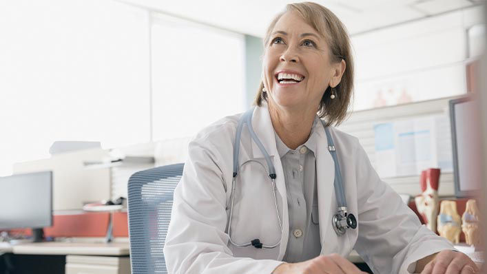 A female doctor smiles while chatting with a patient in her office.