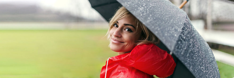 A woman walking in the rain smiles at the camera from under an umbrella.