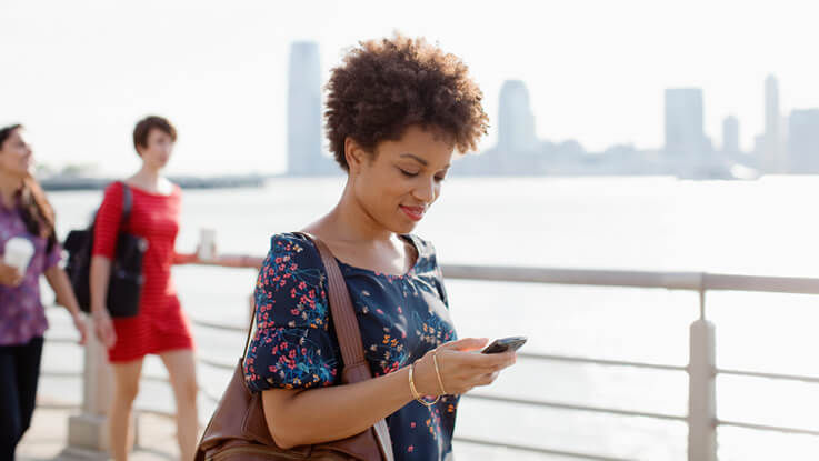 Woman walking outside, smiling and looking down at her mobile phone.