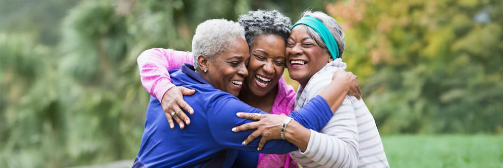A group of three women standing in a circle, smiling and hugging.