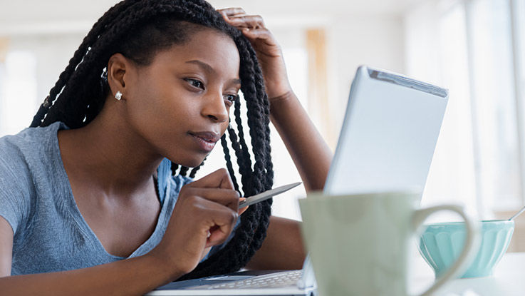 A woman reads information from her laptop at home as she takes notes