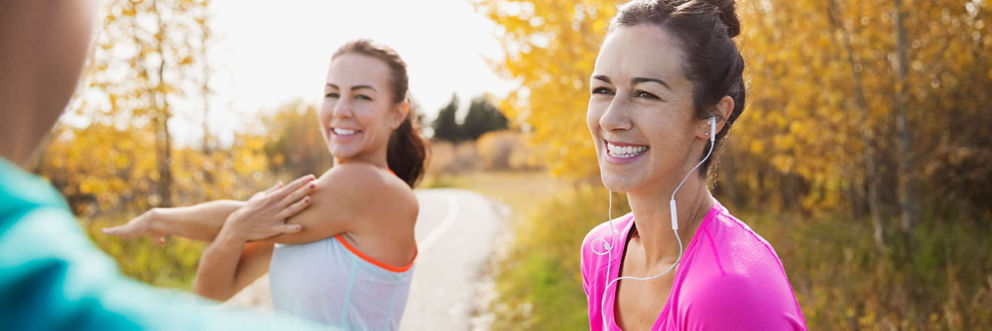 Two women smile and stretch while talking with a friend before a run outdoors.