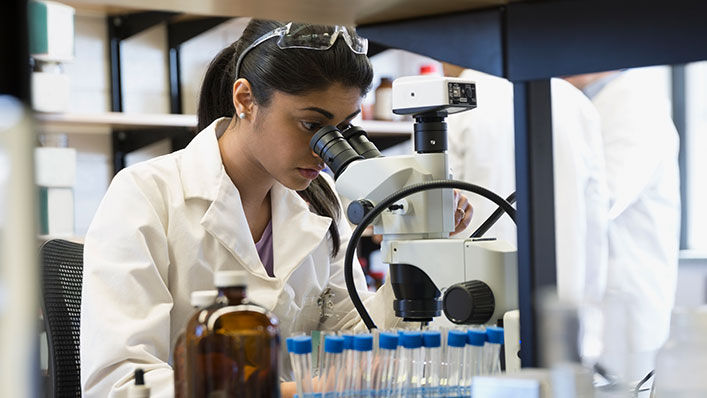 A young female doctor studies a sample through a microscope in the lab.