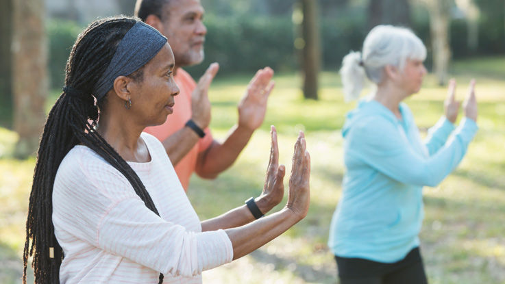 In a park on a sunny day, three adults practice tai chi