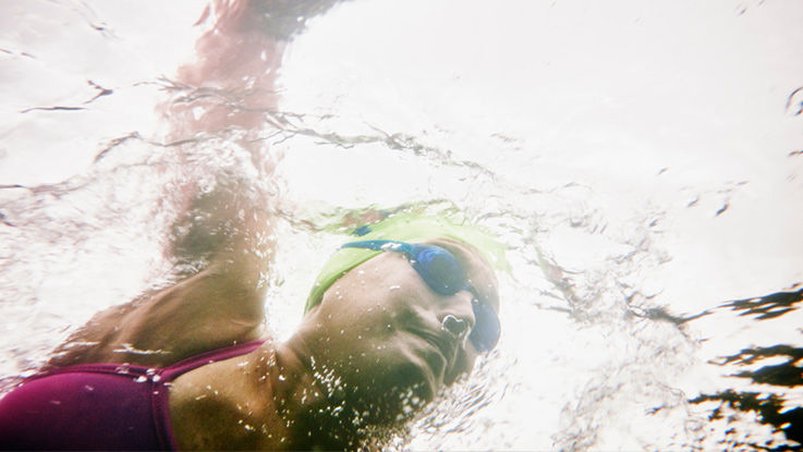 Wearing a cap and goggles, a woman swims laps in a swimming pool.