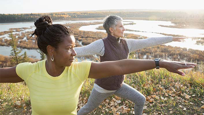 Two women practice yoga in a serene outdoor setting.