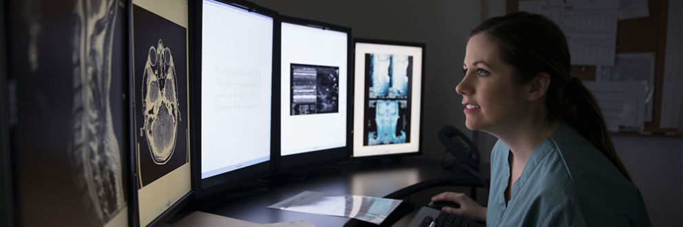 A doctor reviews MRI scan results on multiple computer screens.