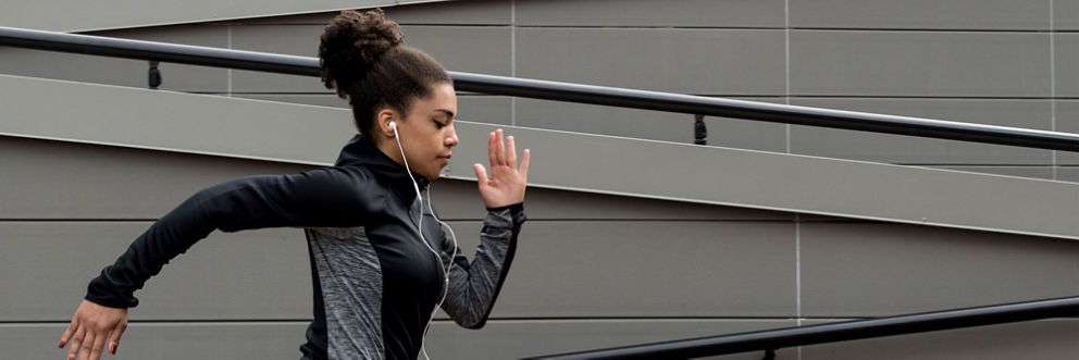 A young woman wearing earbuds is mid-sprint.