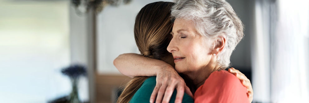 An older woman closes her eyes as she hugs a young woman.