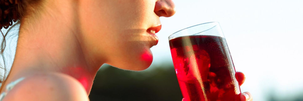 A woman drinking a glass of cranberry juice.