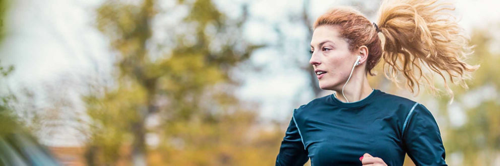 A young woman wearing earbuds and with a bouncing ponytail goes for a jog outside.