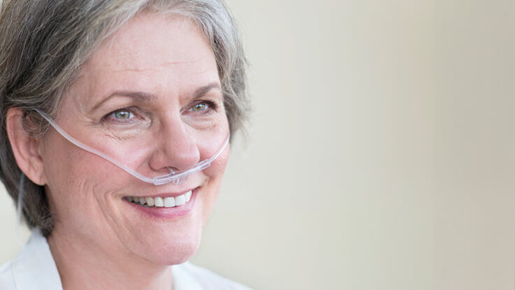 Wearing an oxygen nose tube, an older woman smiles.