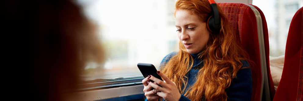 A young woman wearing headphones rides the train and looks at her phone.