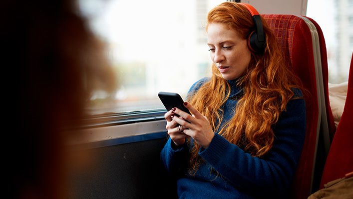 A young woman wearing headphones rides the train and looks at her phone.