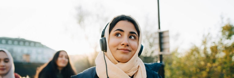 A woman wearing headphones and listening to music on her walk with friends.
