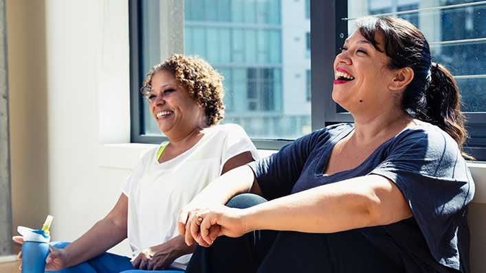 Two women laugh during a break at an exercise class.