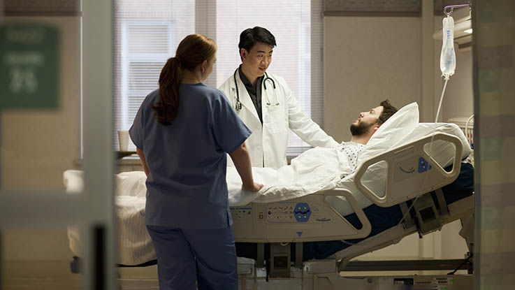 A doctor and nurse check on a patient in his hospital room. 