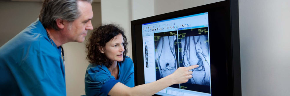 Doctors looking at large computer monitor with MR scan image of human knee.