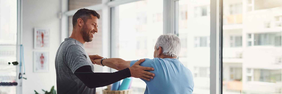 A physical therapist helps a patient complete a shoulder strengthening exercise.