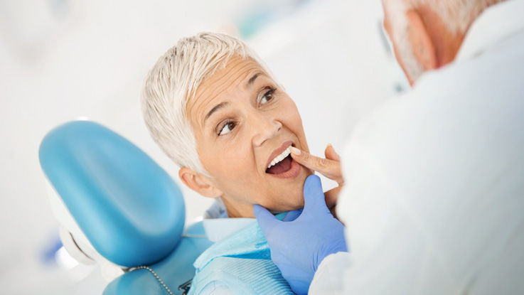 Sitting in an exam chair, an older woman points out a front tooth to her dentist.