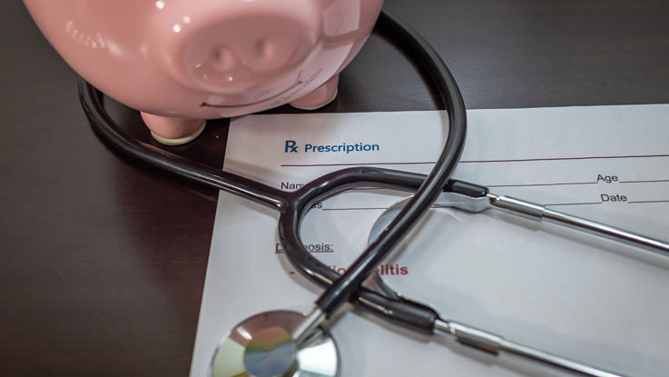 A stethoscope, prescription pad and piggy bank sitting on a table.