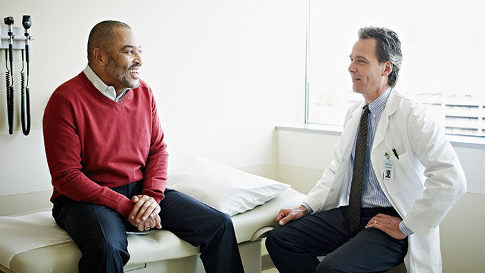 A man in a medical exam room speaks with a doctor about his health