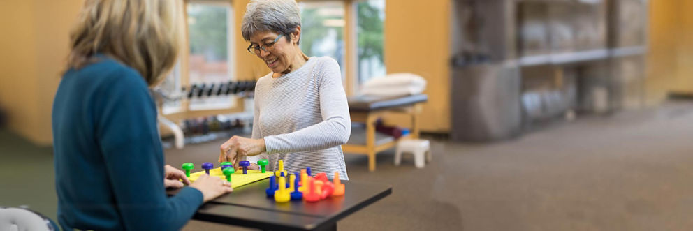 An older patient works on fine motor skills by playing a game with her occupational therapist.