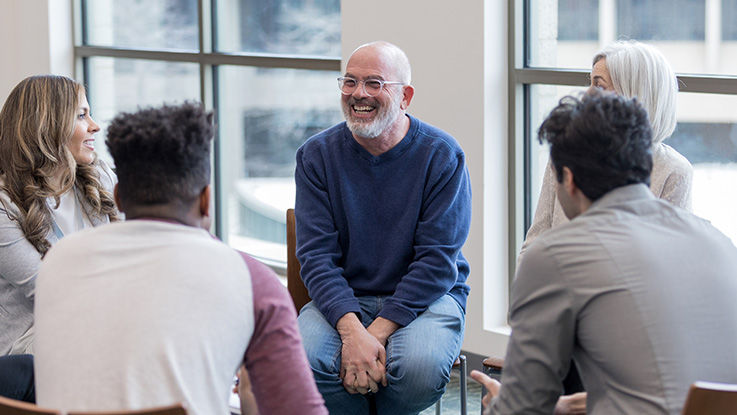 A man smiles as he talks with the other folks seated around him at a support group.