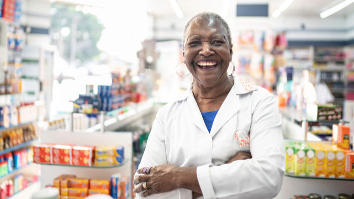 A friendly pharmacist stands in an aisle of her pharmacy.