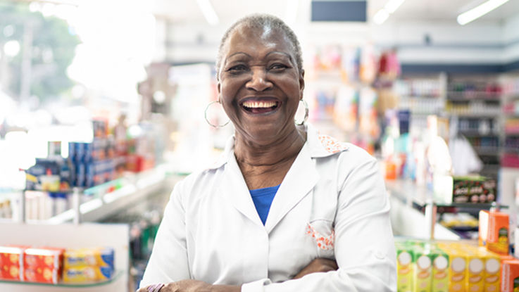 A friendly pharmacist stands in an aisle of her pharmacy.