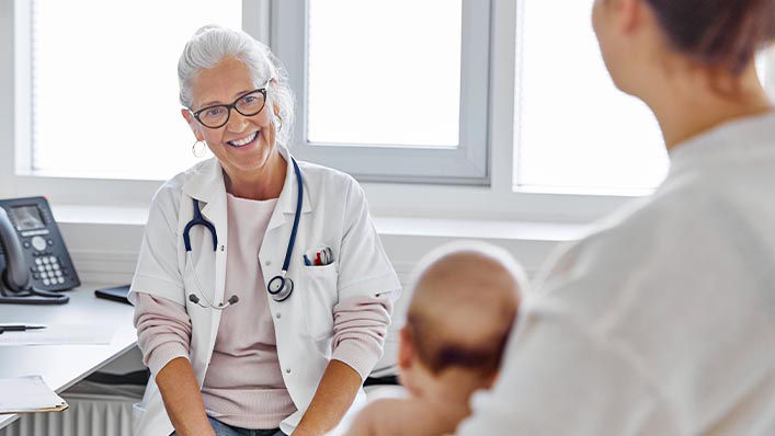 A smiling doctor speaks with a mother about her newborn baby at a checkup.