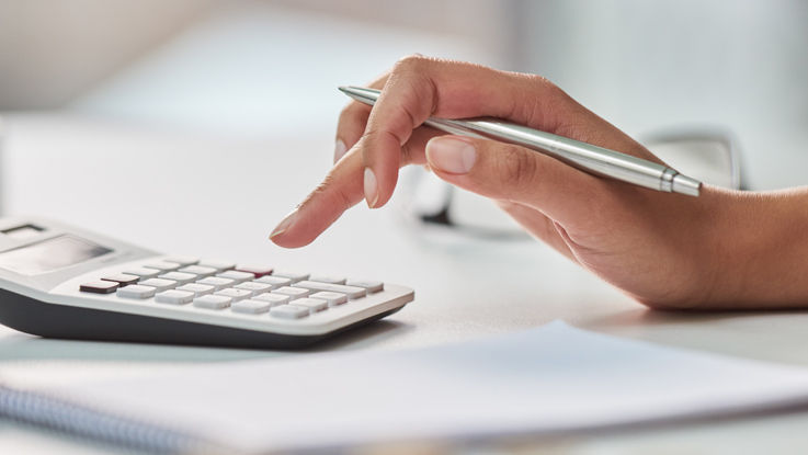 Hand holding a pen and punching numbers into a calculator.