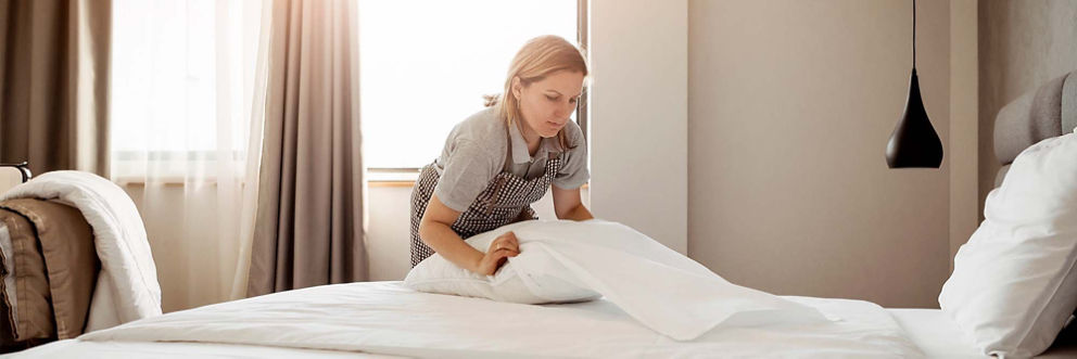 A hotel employee changes the sheets on a bed.