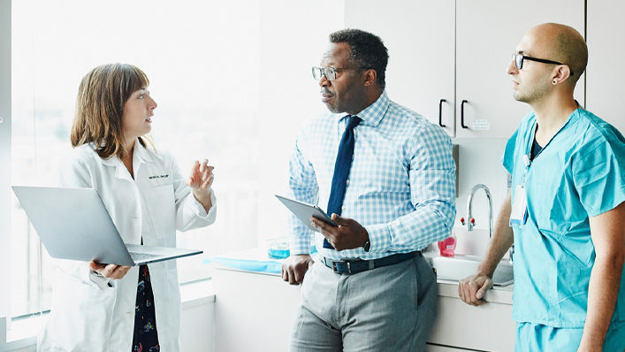 A doctor discusses something on her open laptop with two other clinicians.