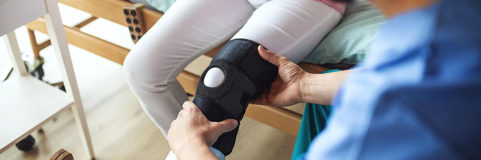 A physical therapist helps a patient move their knee in a knee brace.