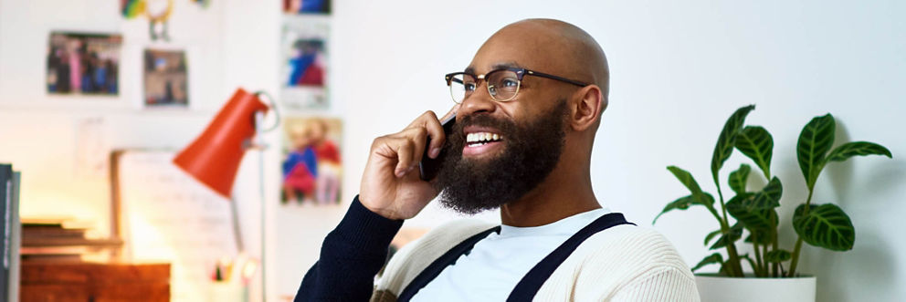 A man sitting in his home office grins as he speaks on the phone