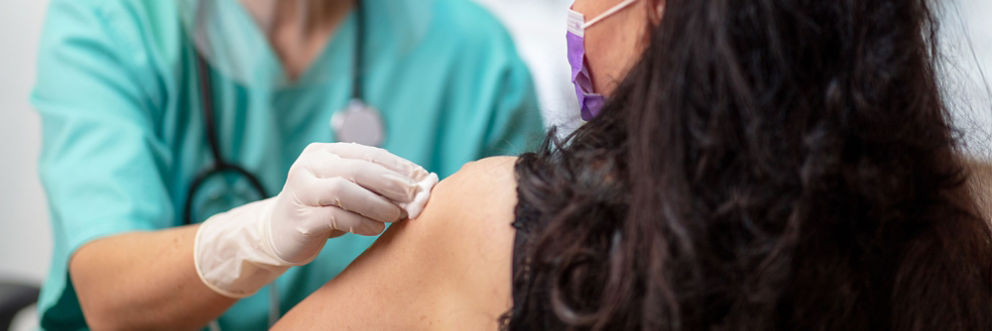 A nurse cleans the injection site on a woman's arm before giving her a shot.