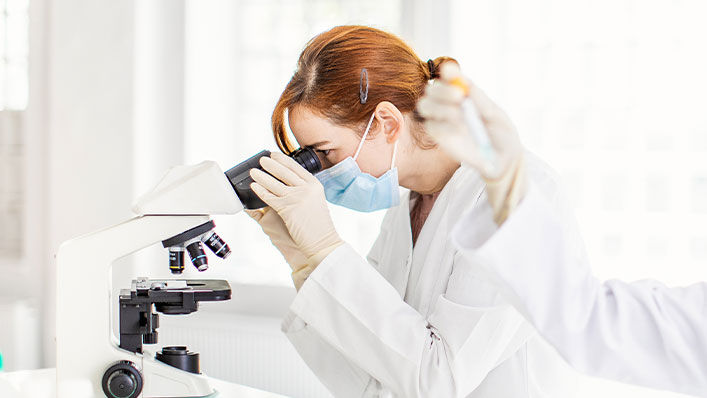 A female researcher studies a sample through a microscope at a lab.